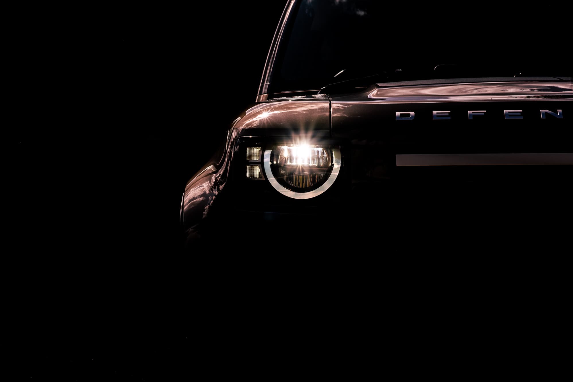 Close-up of a Land Rover Defender headlight catching golden sunlight