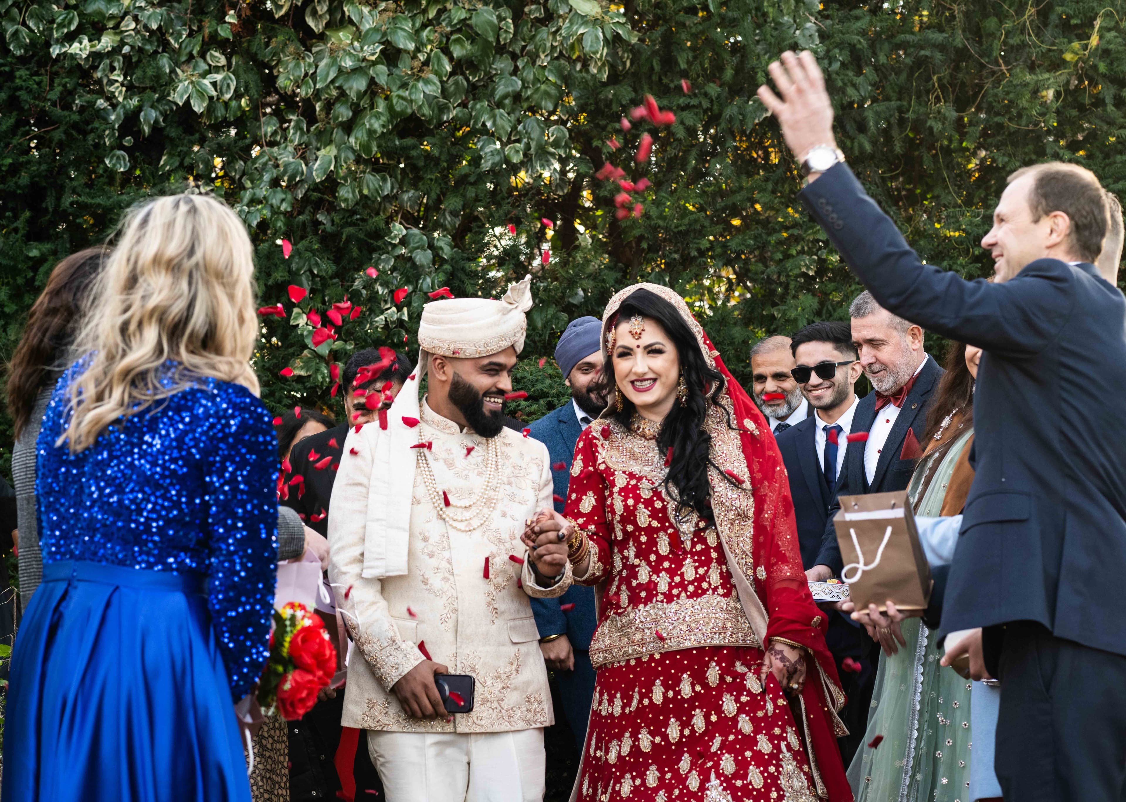 A joyful bride and groom walk together with rose petals in the air