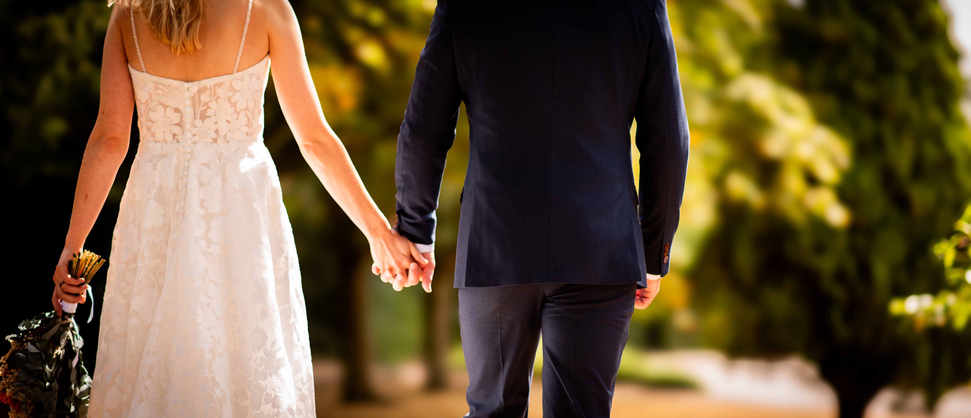 Bride and groom holding hands as they walk together in golden sunlight