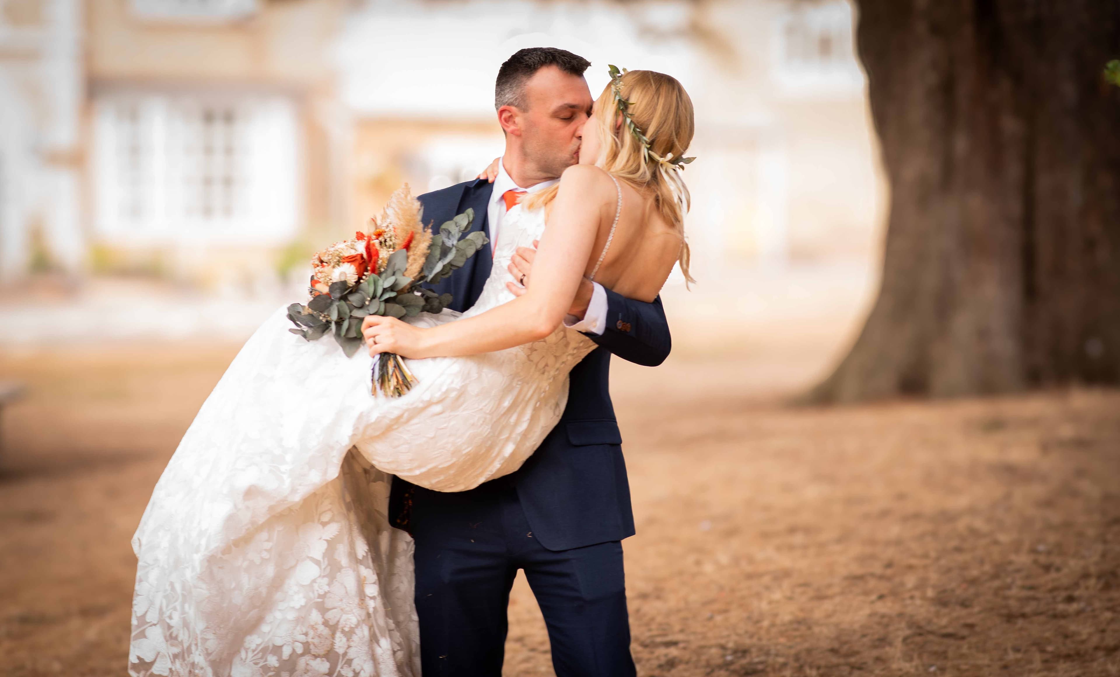 Groom carrying his bride in his arms as they share a kiss