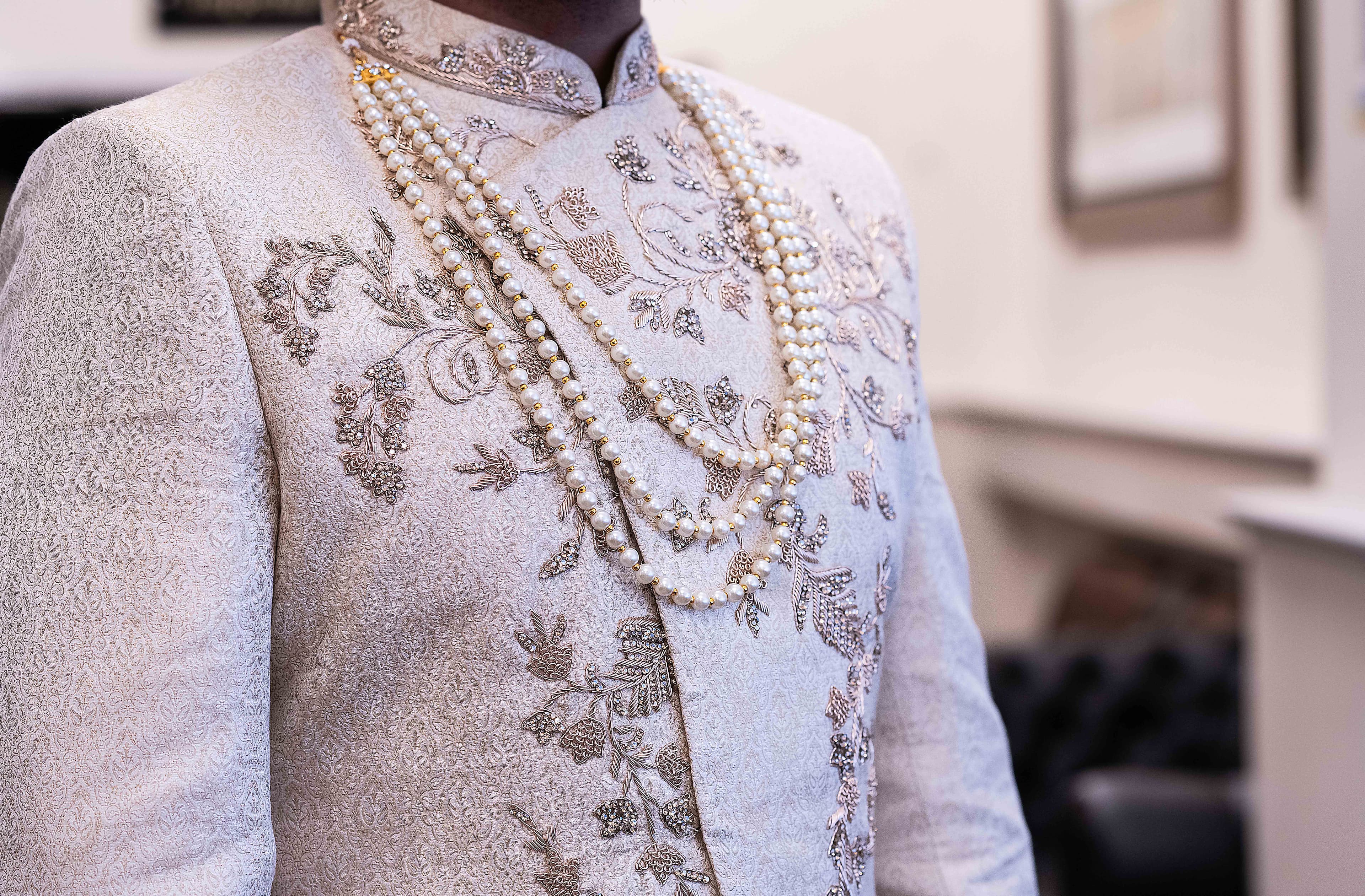 Pearls hang around the groom's neck and chest